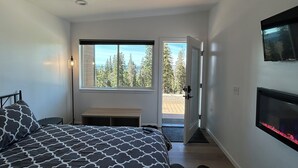 A bedroom with a bed, a bench, a fireplace, a TV, and a view of trees through a window. - Eagle Point Resort (Beaver)