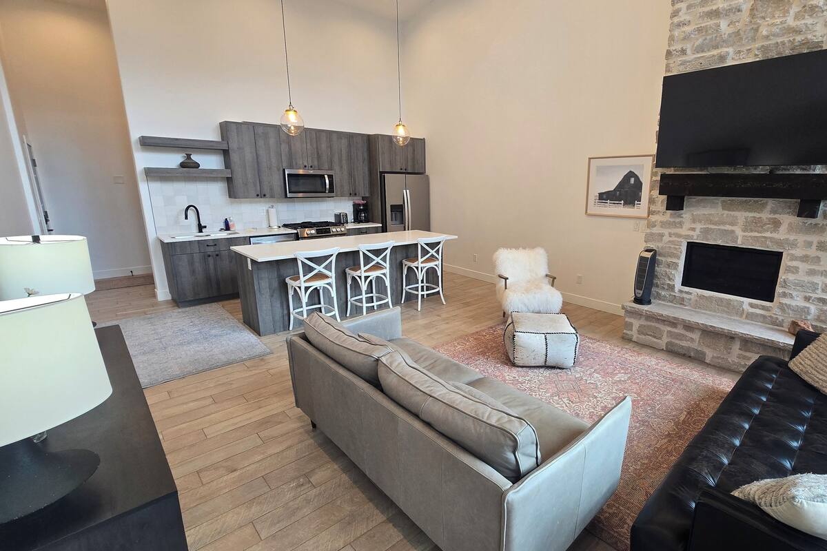 A modern living room with a grey sofa, a black leather couch, and a kitchen area with a built-in oven and microwave.