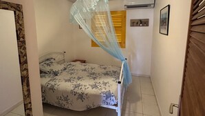 A bedroom with a bed under a mosquito net, a door, and a wall-mounted air conditioner. - AN ANVI, vacation home 400m from the sea (Sainte-Anne)