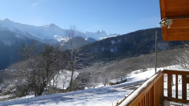 Un balcon en bois offrant une vue sur des montagnes enneigées et un ciel dégagé.