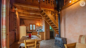 Un intérieur en bois comprenant une table à manger, des chaises, un canapé, un escalier et un poêle à bois.