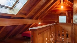 Une pièce mansardée en bois, avec un puits de lumière, une petite fenêtre et un luminaire.