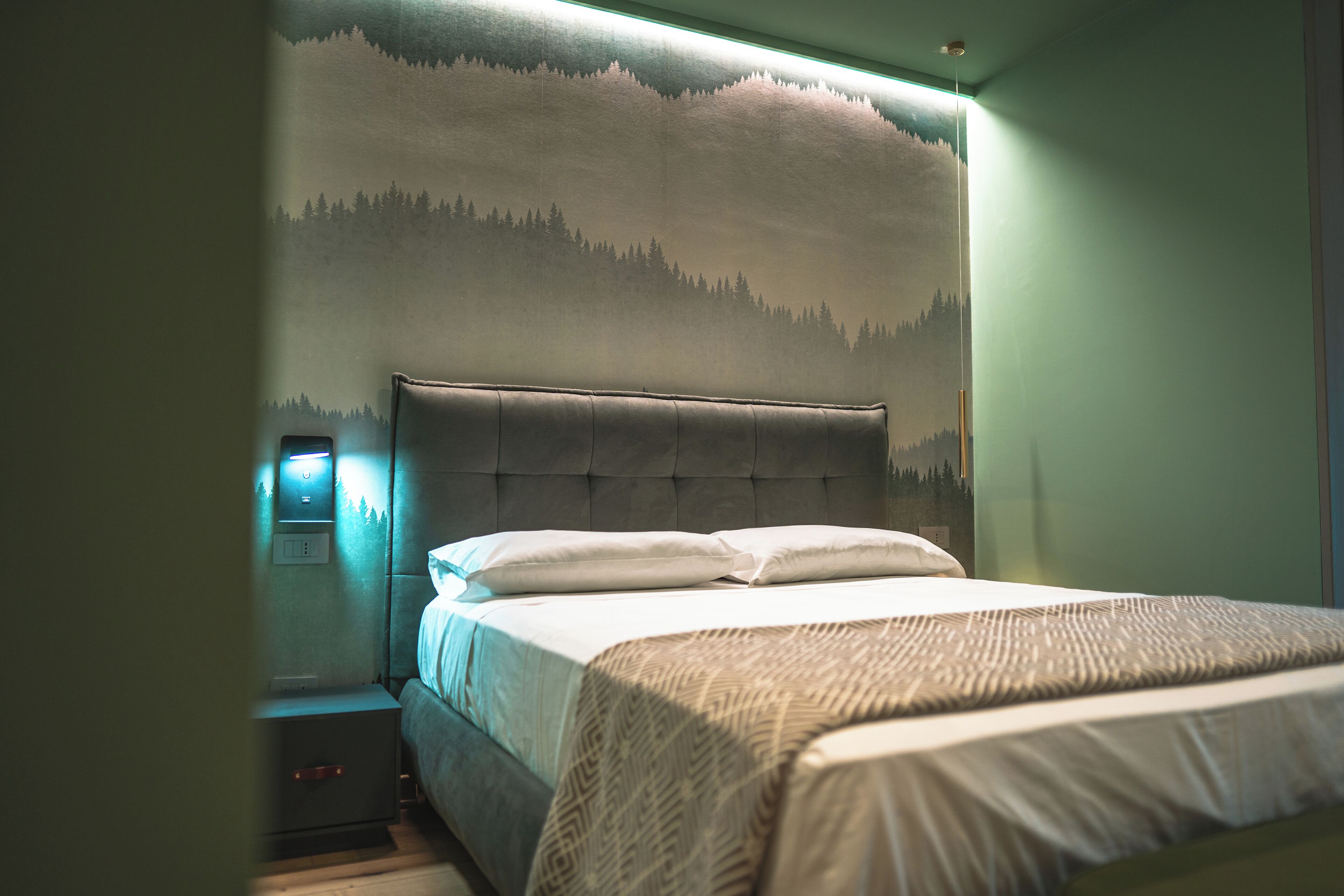 Ein Schlafzimmer mit einem großen Bett, einem Nachttisch und einer Wandmalerei von einem Wald.