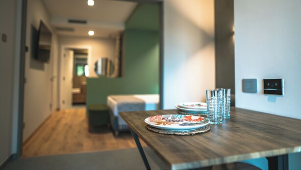A modern dining area with a wooden table set for two, featuring decorative plates and clear glasses. - Il Piccolo Paradiso - Magnolia - by Be Your Home (Civitavecchia)