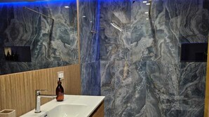 Een moderne badkamer met een marmeren spatwand, een houten wastafelmeubel, een grote spiegel en een douchehoek.