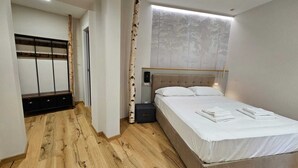 Een moderne slaapkamer met een houten vloer, een bed met witte lakens, een hoofdbord met een bosdecoratie, en een bankje met haken.