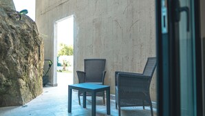 Een terras met twee rieten stoelen en een tafel, een grote rots en een betonnen muur.