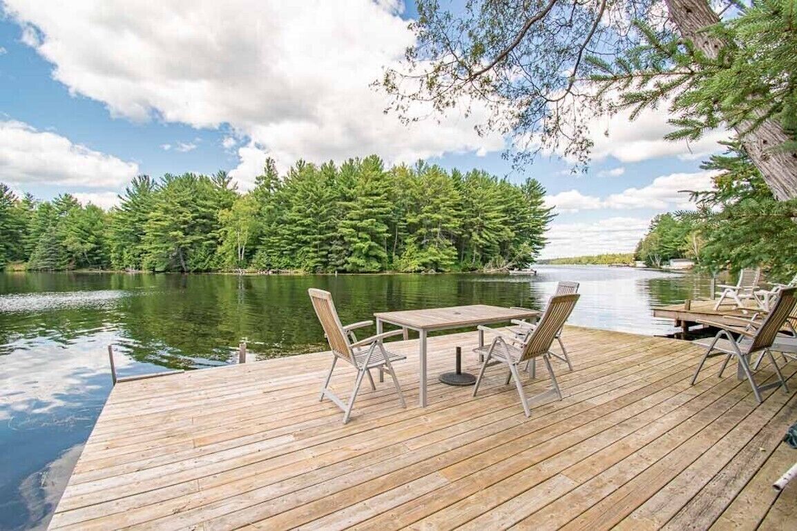 A wooden deck with a table and chairs overlooking a lake surrounded by trees.