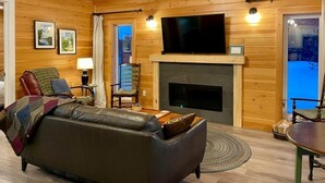 Ein gemütliches Wohnzimmer mit einer Ledersofa, einem Kamin, einem Fernseher und Holzwänden.