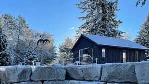 Eine Holzblchütte mit einer Steinwand im Vordergrund, umgeben von schneebedeckten Bäumen.