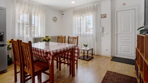 Un comedor con mantel a cuadros, sillas de madera, una mesa pequeña con un florero y un refrigerador.