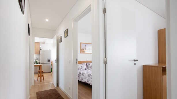 Un pasillo que conduce a un dormitorio con una cama, un armario de madera y una cocina al fondo.