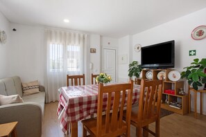 Una sala de estar con una mesa a cuadros, sillas de madera, un sofá, un televisor y una planta.