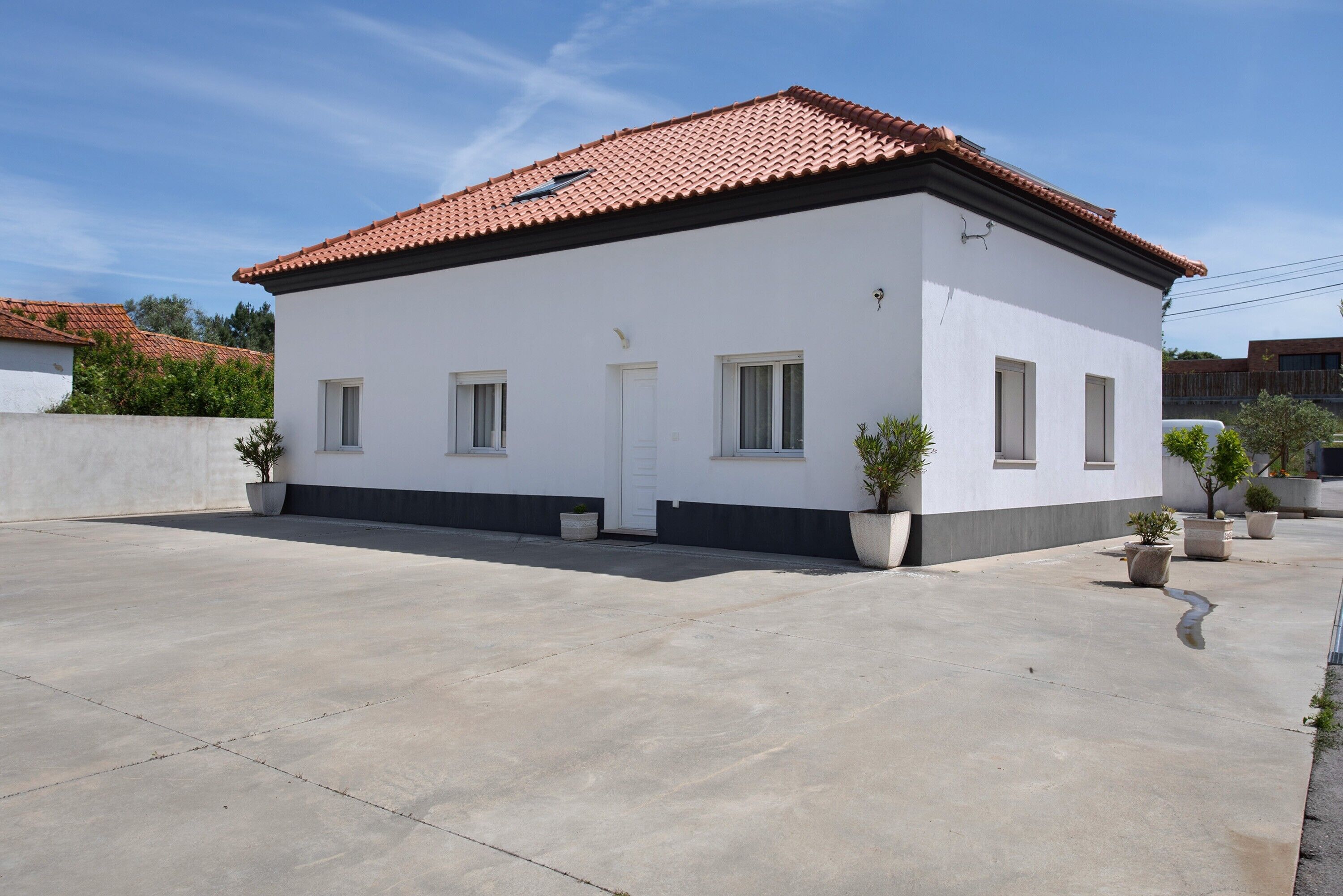 A single-story building with a red-tiled roof, white walls, and a concrete driveway.