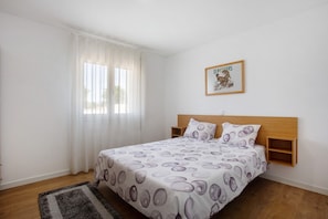 Un dormitorio con cama, una ventana con cortinas, cabecera de madera y un cuadro enmarcado en la pared.