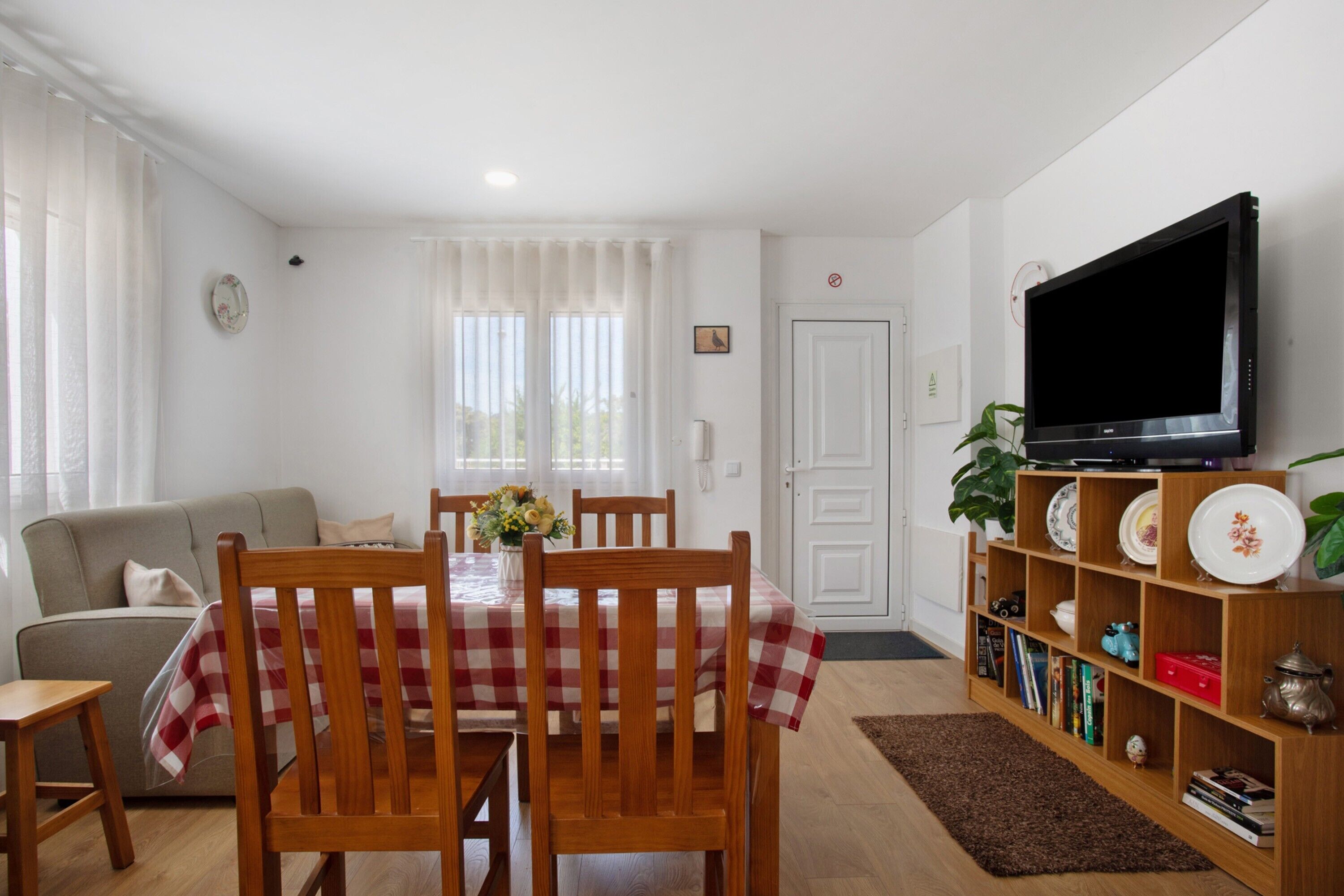 Zona pranzo con tavolo apparecchiato per quattro, televisore su un mobile e libreria con oggetti decorativi.