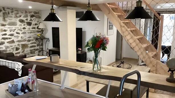 Una cocina moderna con pared de piedra, escalera de madera e iluminación colgante.