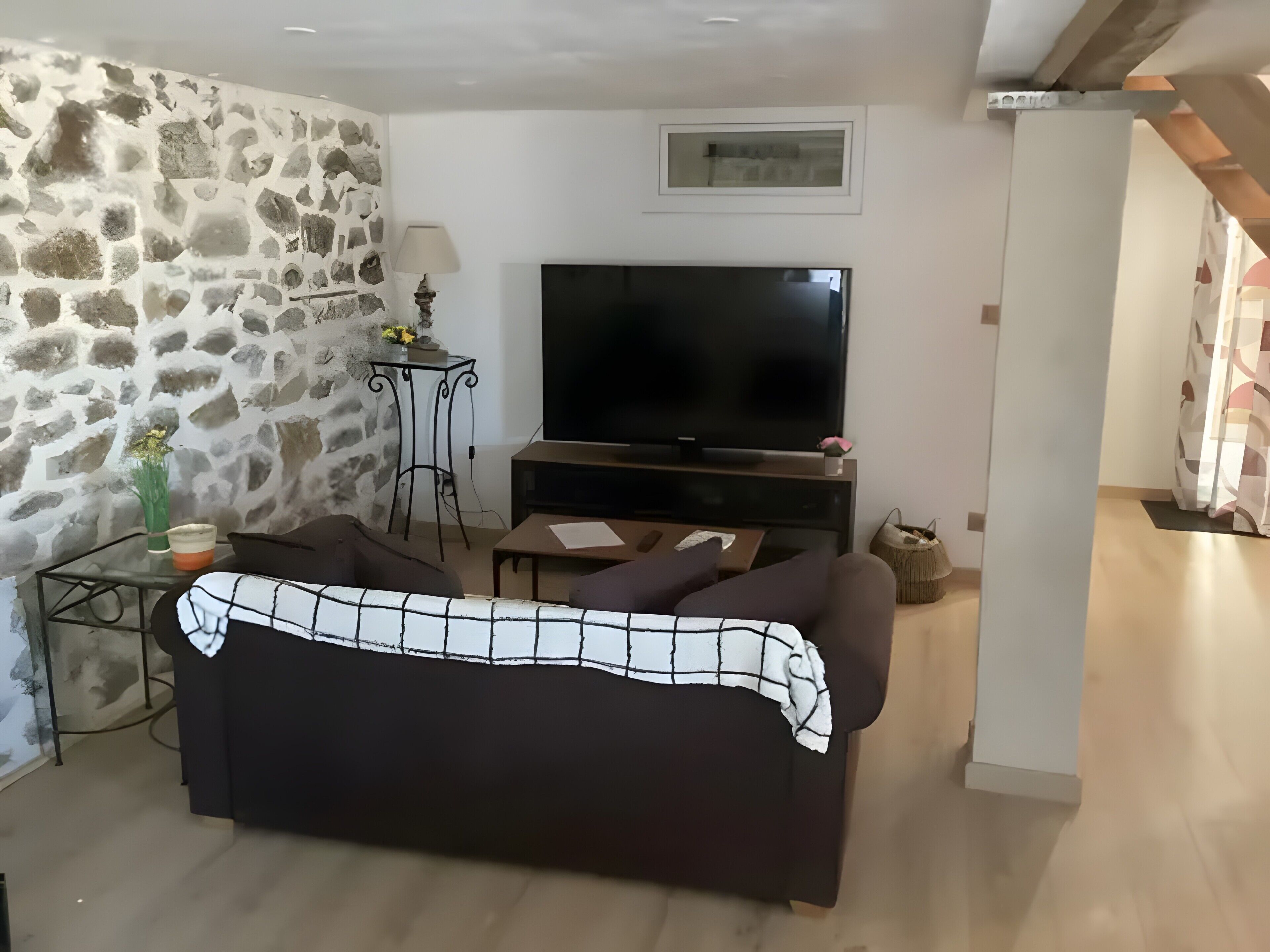 A living room with a stone wall, a sofa, a TV, a small table, and a lamp.
