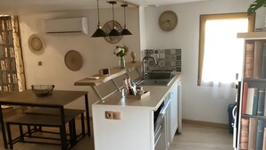 Una cocina moderna con una isla central, luces colgantes, un reloj y una ventana con persianas.