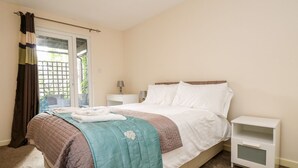 A bedroom with a bed, a nightstand, a lamp, and a window with curtains. - Valley Lodge 31 (Gunnislake)