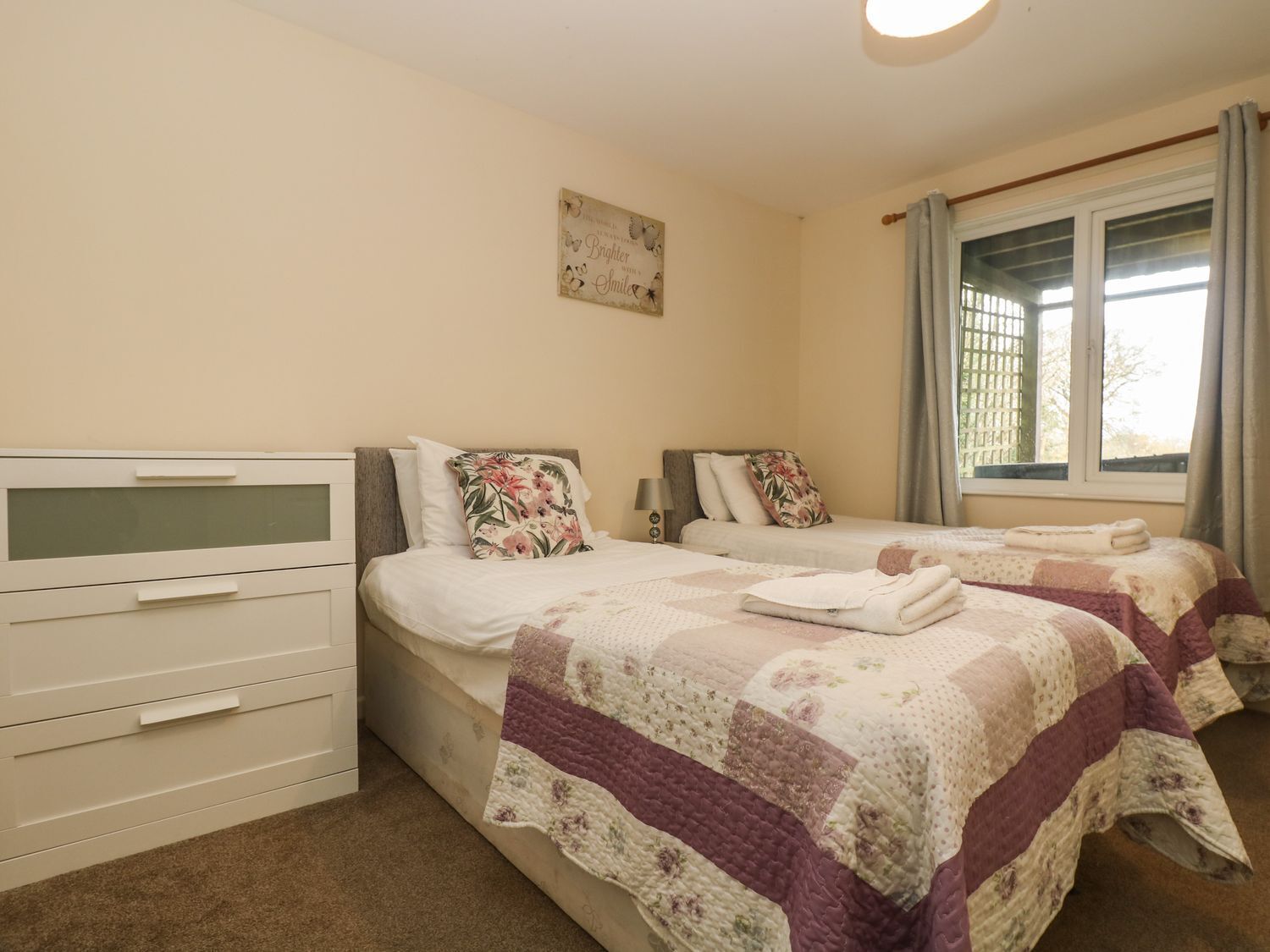 A bedroom with two beds, a dresser, a bedside table, and a window with curtains.