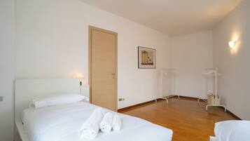 A hotel room with a bed, a wooden door, a wall-mounted picture, and a clothing rack.
