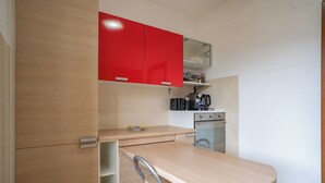 Uma cozinha compacta com bancada de madeira, um armário vermelho, uma cafeteira e um forno pequeno.