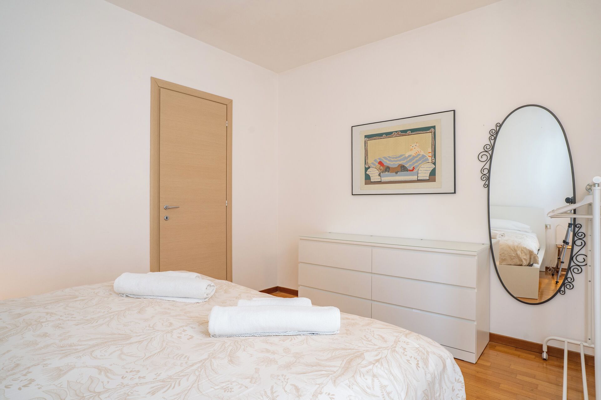 Une chambre à coucher avec un lit, une commode, une porte et un tableau encadré au mur.