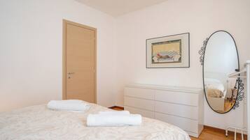 Une chambre à coucher avec un lit, une commode, une porte et un tableau encadré au mur.