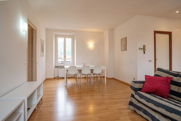A spacious living area with a dining table and chairs, a sofa with a red pillow, and a large window providing natural light. - Manzoni Loft - Two Bedroom Apartment, Sleeps 5 (Galbiate)