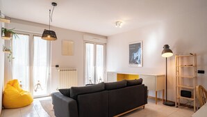A modern living room with a sofa, a yellow bean bag, a floor lamp, and a radiator.