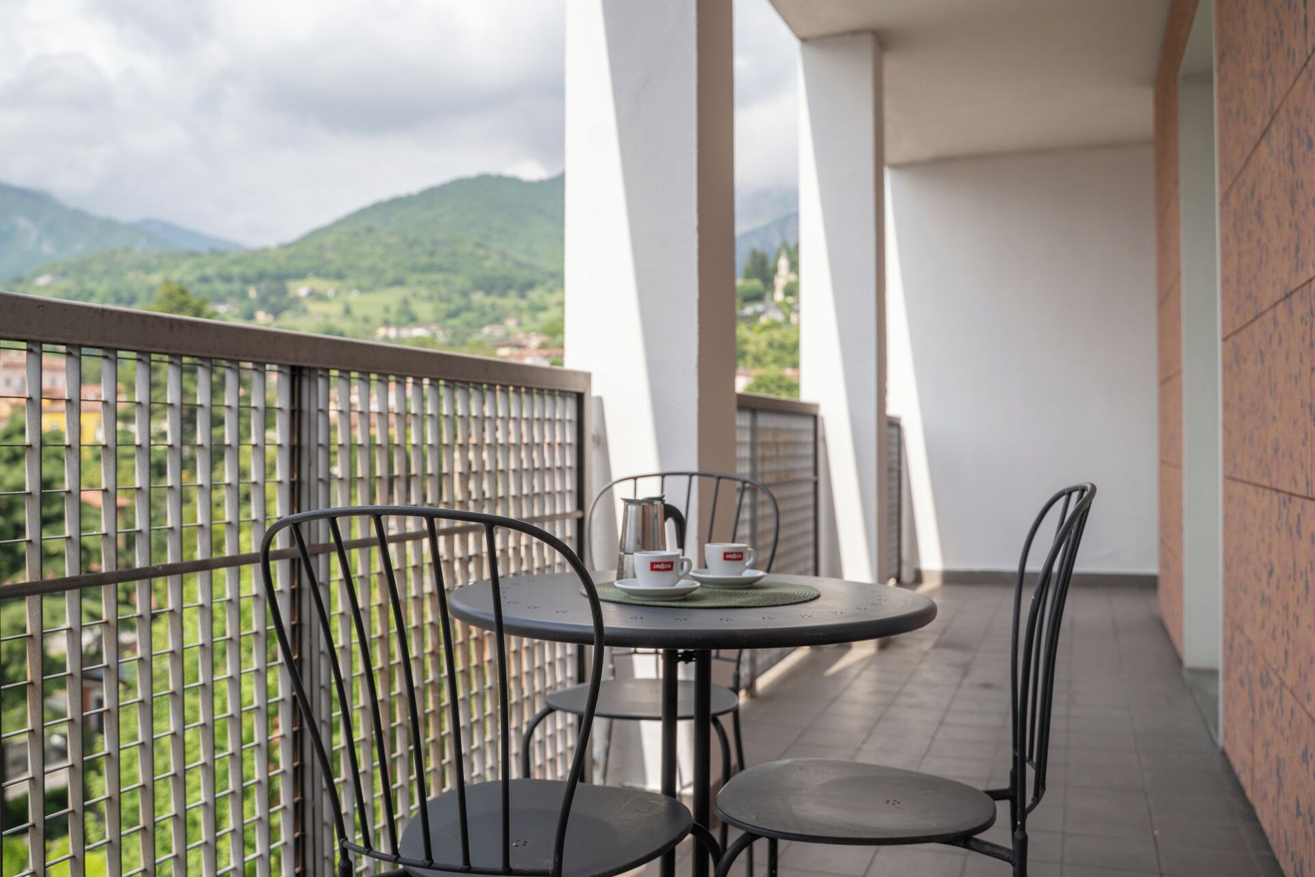 A balcony with two chairs, a table, and a view of green hills.