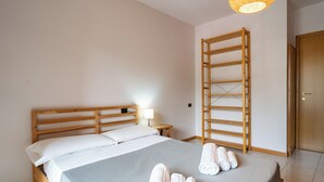 A neatly made bed with white linens and towels, a wooden headboard, a bedside table with a lamp, and a wooden ladder against the wall.