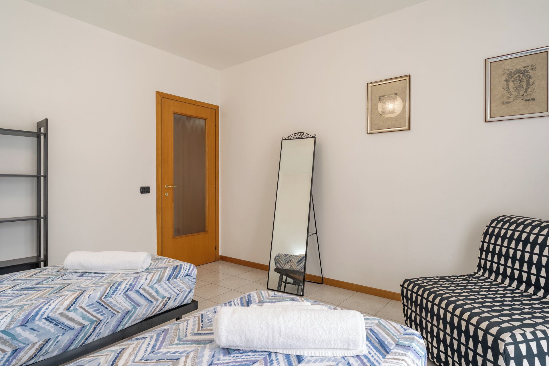 A bedroom with two beds, a wardrobe, a mirror, and a chair.