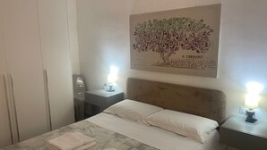 A neatly made bed with pillows, a bedside lamp, and a wall-mounted artwork depicting a tree.