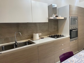 Una cocina moderna con un lavamanos de acero inoxidable, una estufa a gas, un horno empotrado y un microondas.