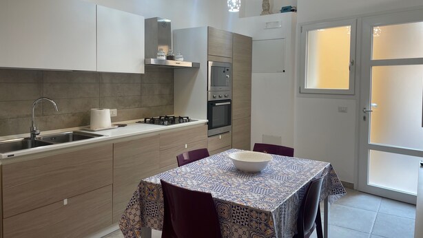 A modern kitchen with a gas stove, sink, and built-in oven. There is a dining table with chairs and a patterned tablecloth.