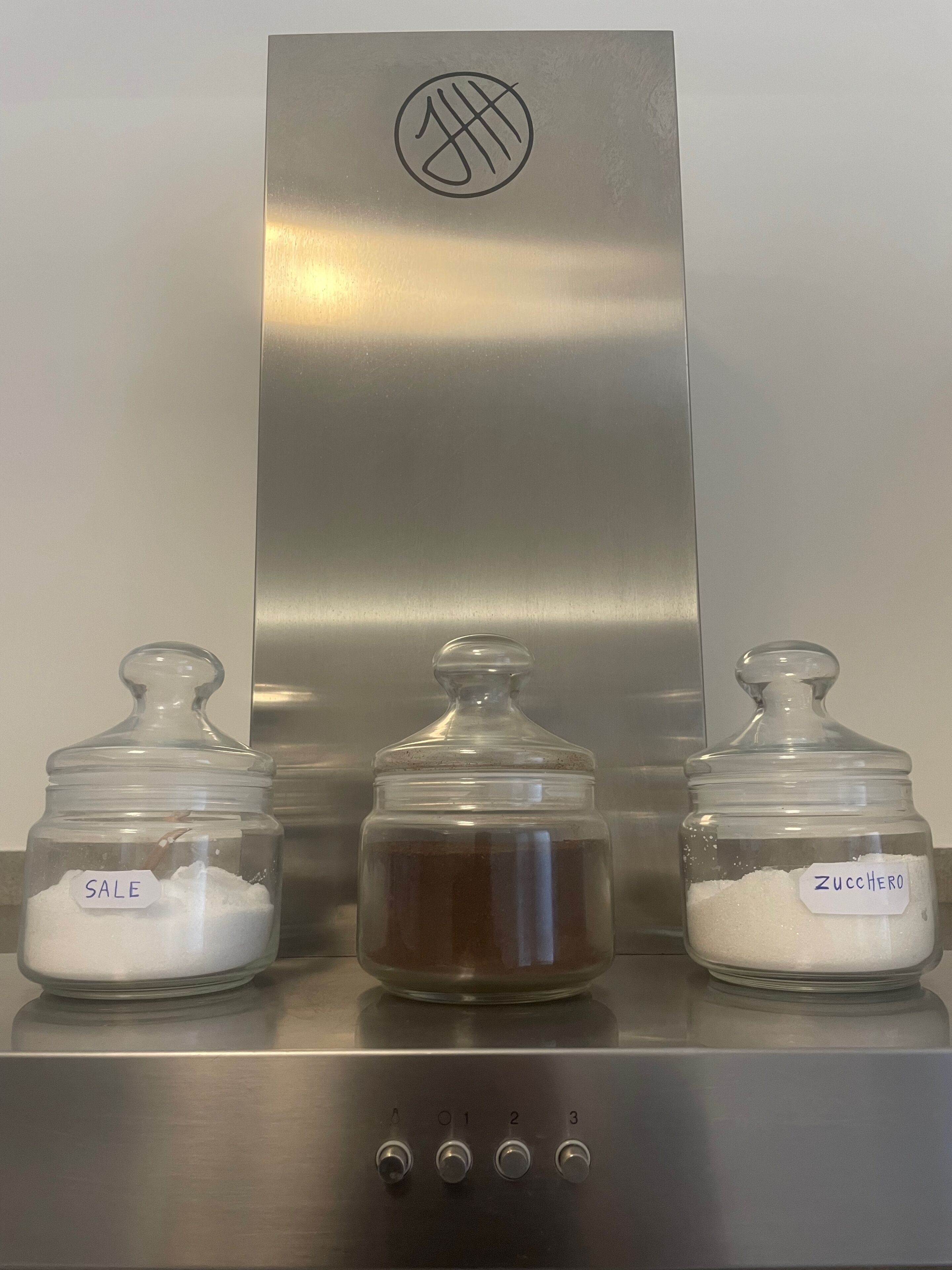 Three glass jars on a stainless steel counter with labels 'SALE,' 'ZUCCHERO,' and 'SALE.'