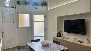 A modern kitchen with a dining table, chairs, a TV, and potted plants.