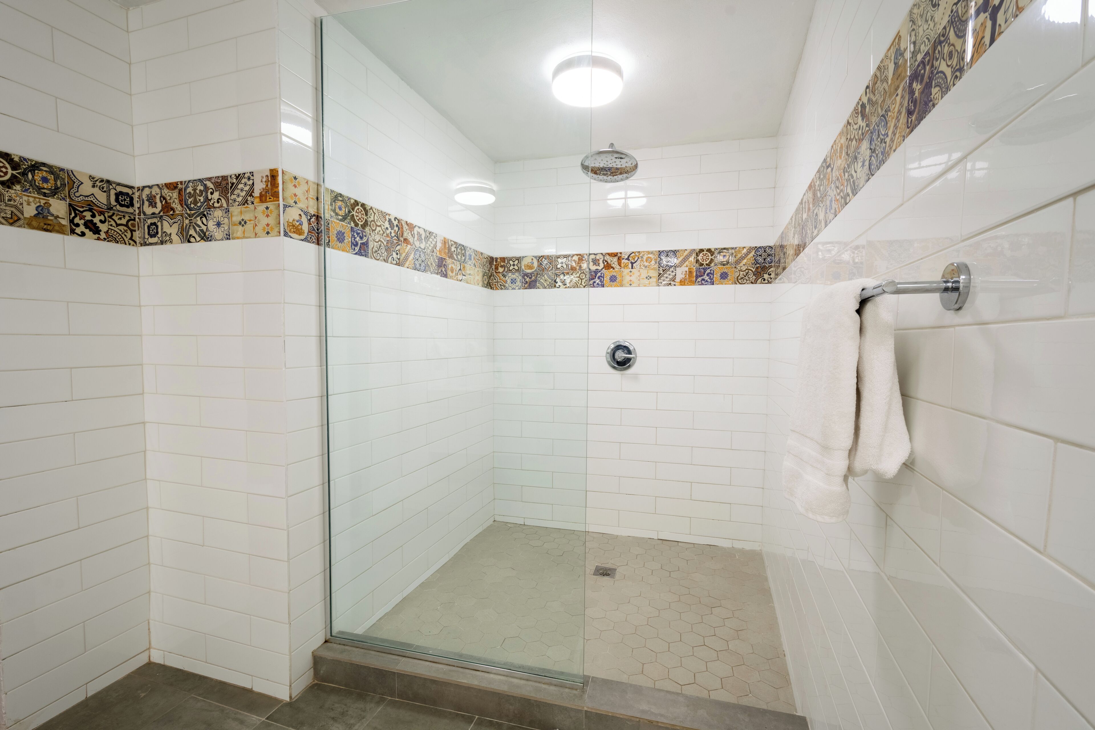 Un baño moderno con azulejos blancos, cabina de ducha con mampara de vidrio y un borde decorativo de azulejos.