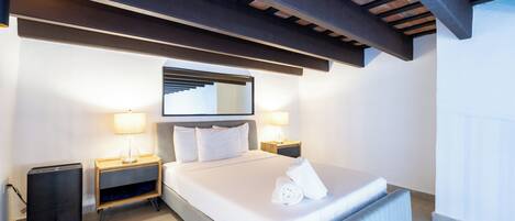 Ein modernes Hotelzimmer mit einem großen Bett, Nachttischlampen, einem kleinen Nachttisch und einem Spiegel an der Wand.
