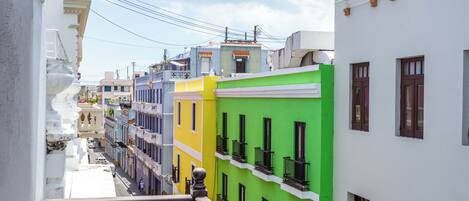 A narrow street with colorful buildings, balconies, and a clear sky.
