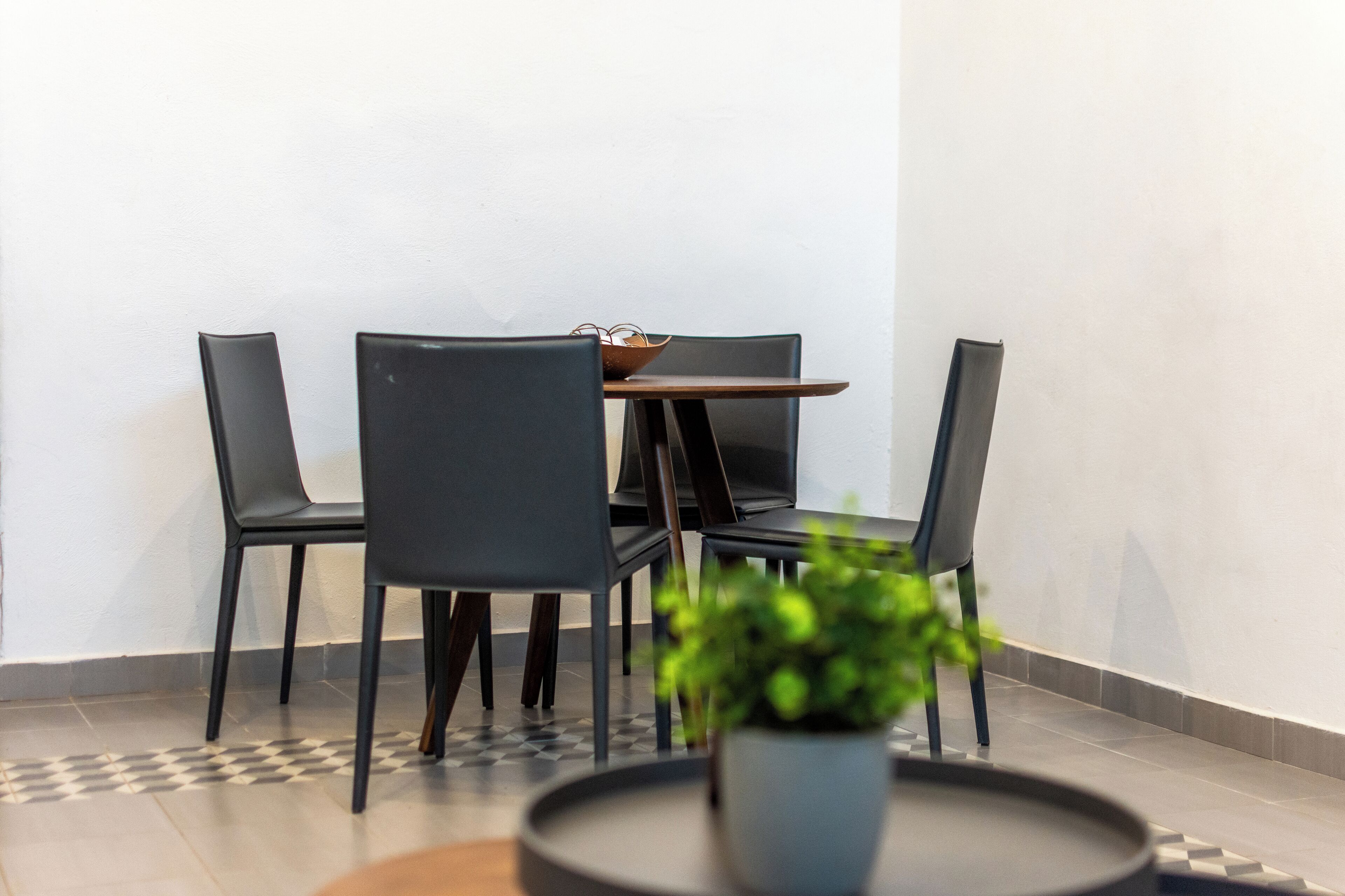 A modern dining area with a table and four chairs, a potted plant, and a checkered floor pattern.