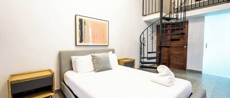 Une chambre moderne avec un grand lit, une table de chevet en bois, un tableau abstrait accroché au mur et un escalier menant à un niveau supérieur.
