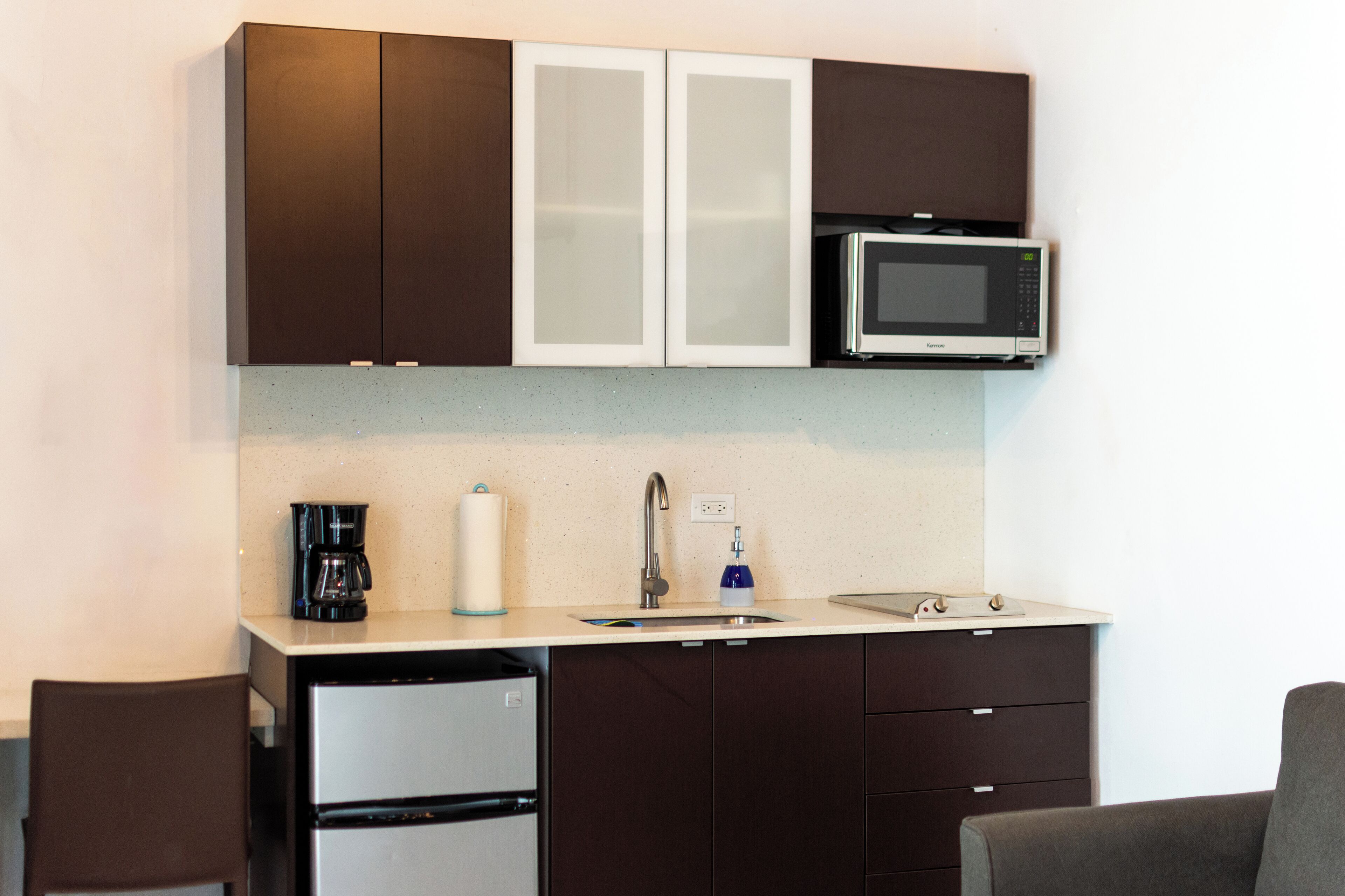 A compact kitchen with dark cabinets, a microwave, a coffee maker, and a sink.