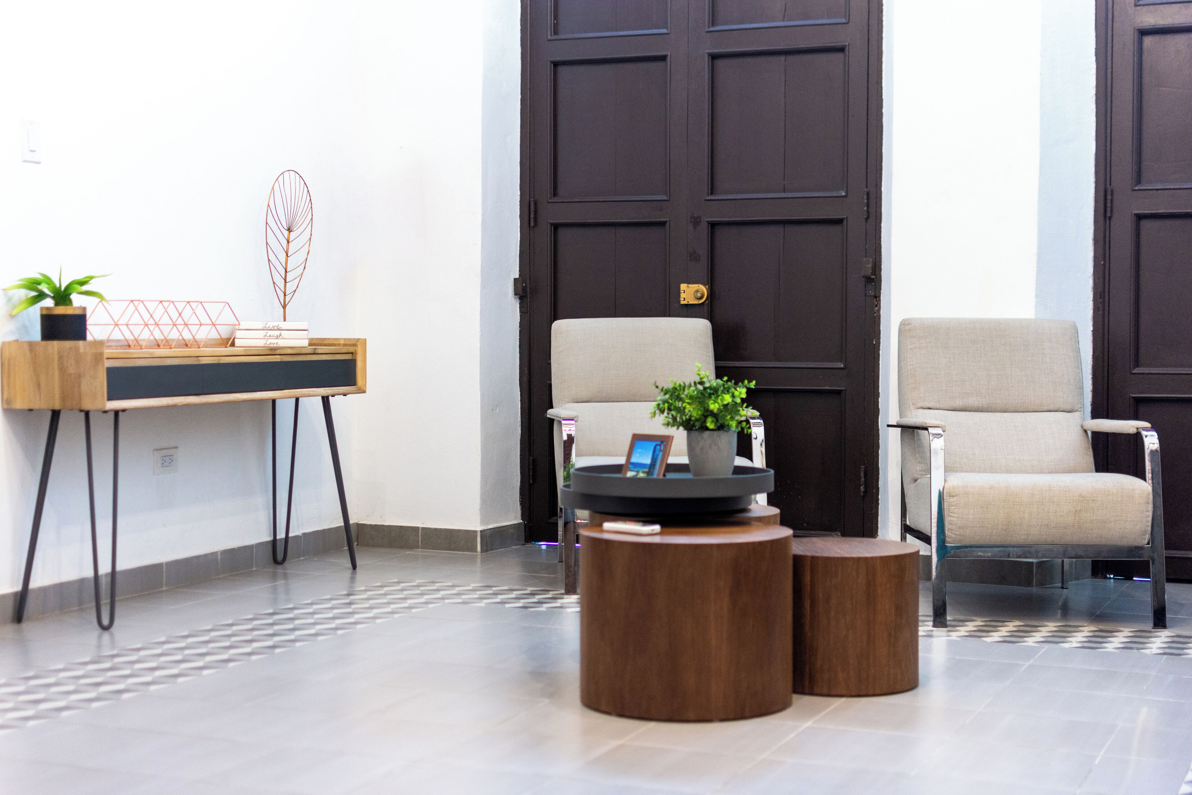 A modern lobby with a wooden desk, two chairs, and a small round table with a plant.