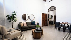 A modern living area with a sofa, armchair, coffee table, and dining table. There is a plant, two wall mirrors, and a kitchen visible through an open door. - 153 Luna by Stay with Bear (San Juan)