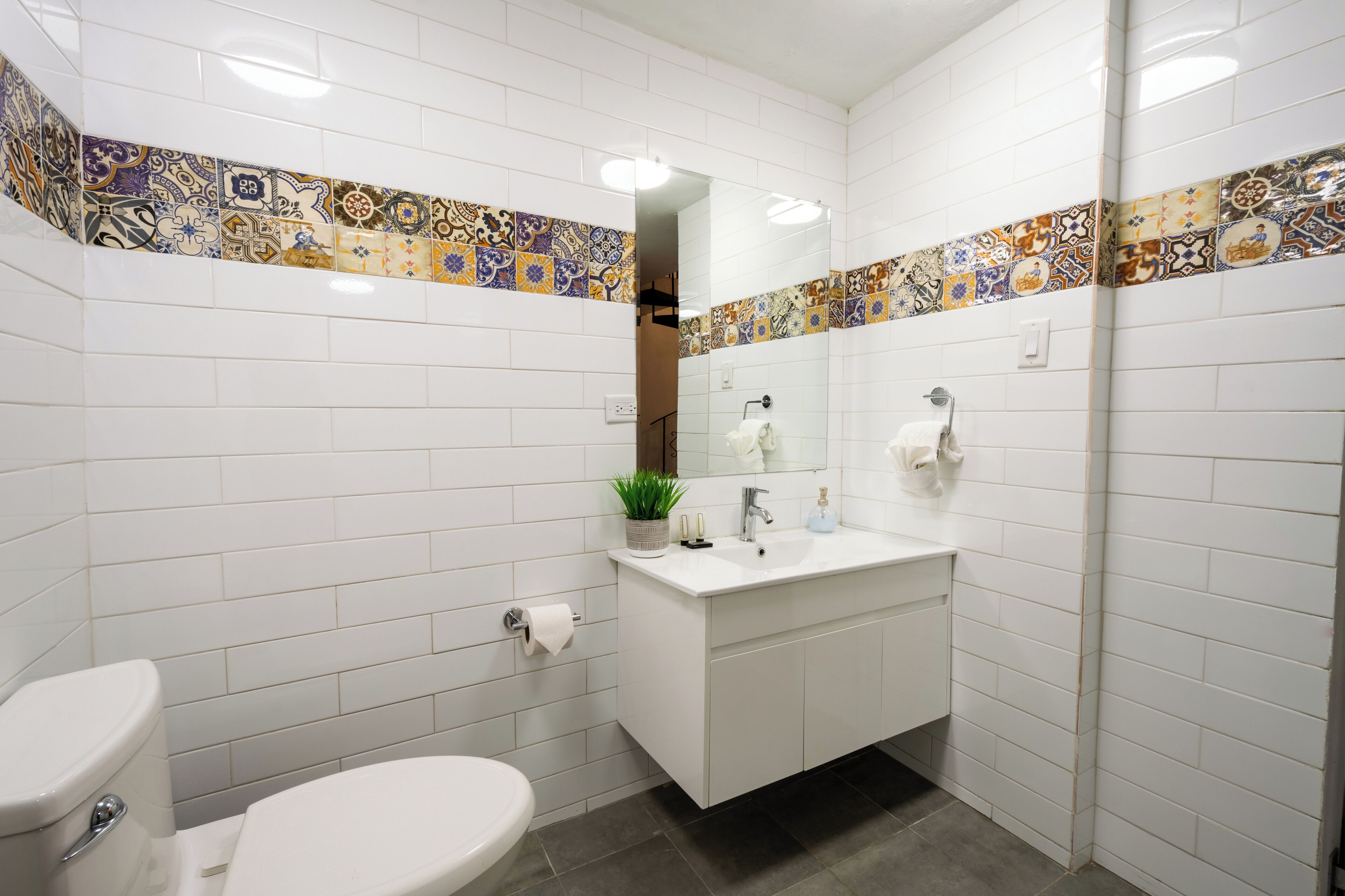 Ein Badezimmer mit weißen Fliesen, einem weißen Waschbecken, einem Spiegel und einer Toilette.
