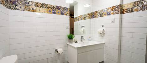 Un baño con azulejos blancos, un lavamanos blanco, un espejo y un inodoro.
