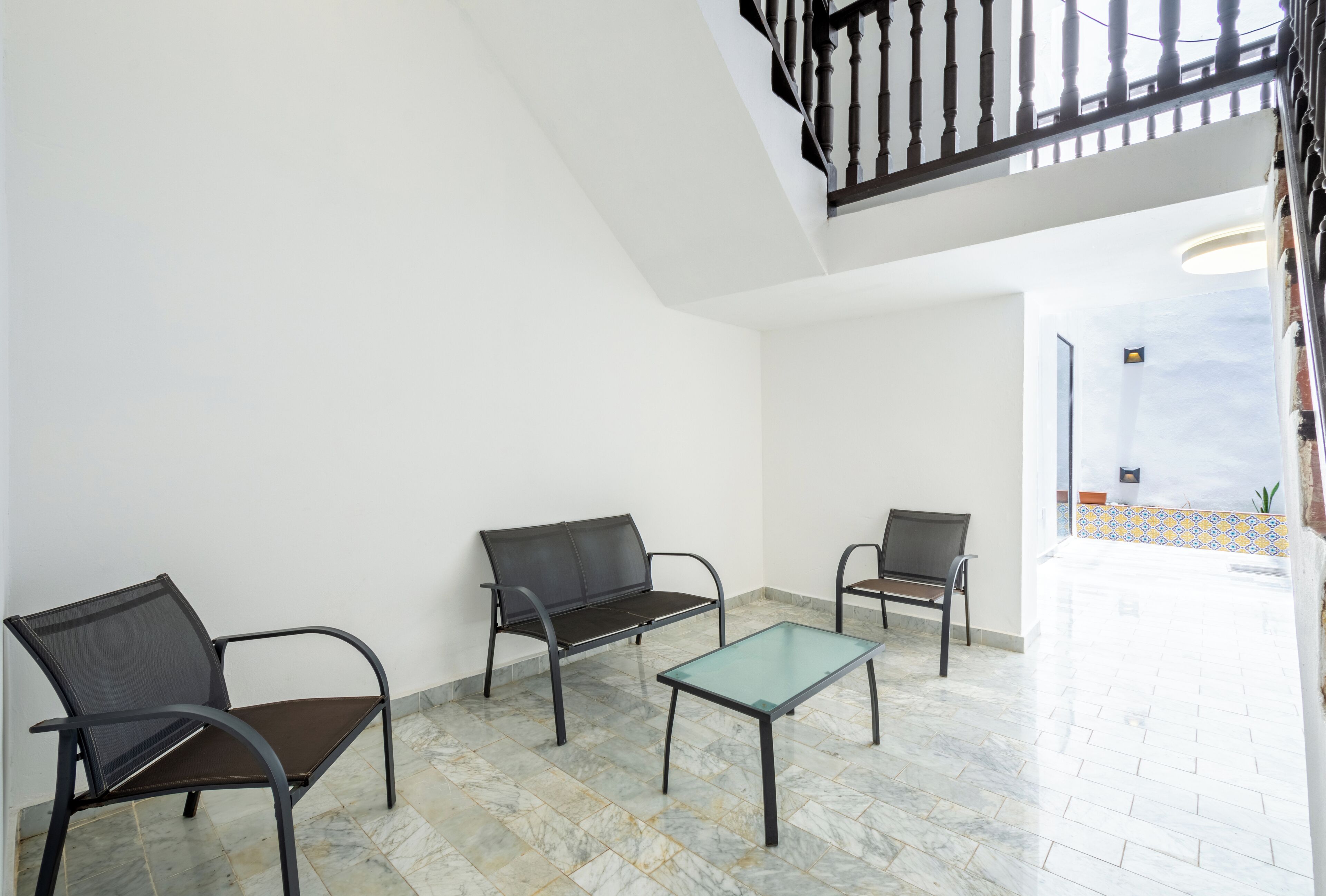 Een ruime kamer met een marmeren vloer, een tafel met een glazen blad en drie donkere stoelen.